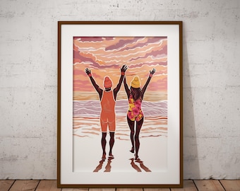 May include: A framed art print depicting two figures standing on a beach with arms raised toward a sunset sky. One figure wears an orange swimsuit and beanie, while the other wears a floral patterned swimsuit and yellow beanie, facing the ocean.