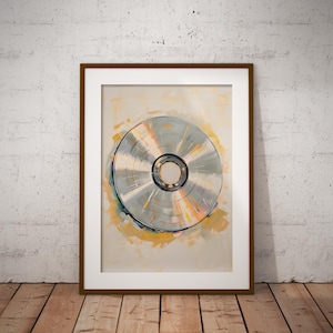 May include: Framed artwork featuring a CD or DVD. The artwork has a silver disc with a central hole, set against a backdrop of soft yellow and orange brushstrokes. The frame is a dark brown color, and the artwork is displayed on a white wall and wooden floor.
