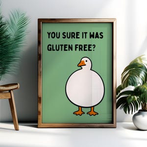 May include: A framed wall art print featuring a round white goose with an orange beak and feet on a sage green background. The text "YOU SURE IT WAS GLUTEN FREE?" is printed in black capital letters above the illustration of the goose.