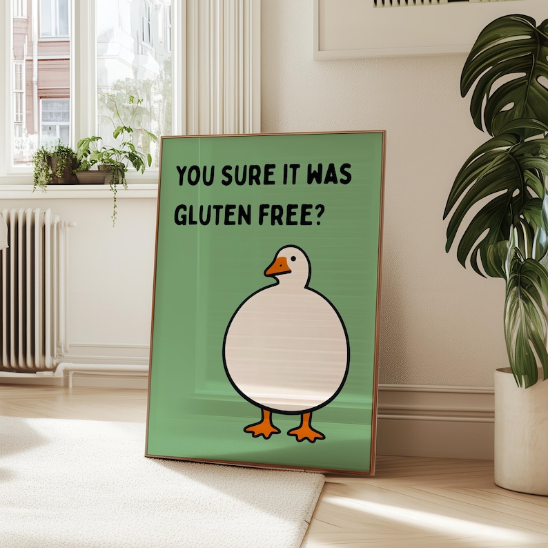May include: A rectangular wall art print featuring a sage green background with a cartoon illustration of a round white goose with orange feet and beak. The black text above the goose reads, "YOU SURE IT WAS GLUTEN FREE?" in a bold font.