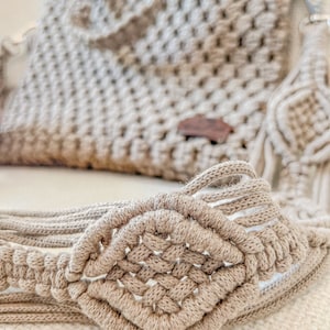 Puede incluir: Primer plano de un bolso de macramé beige con un detalle de nudo en forma de diamante. El bolso está hecho de cordón de algodón natural grueso.