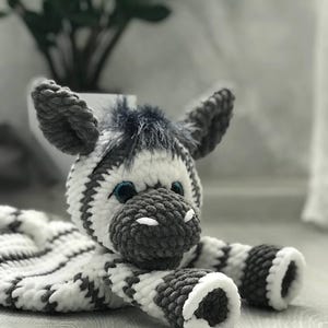 Könnte beinhalten: Ein gehäkeltes Zebra-Plüschtier mit schwarzen und weißen Streifen. Das Zebra hat ein graues Gesicht mit schwarzen Augen und einer weißen Nase.