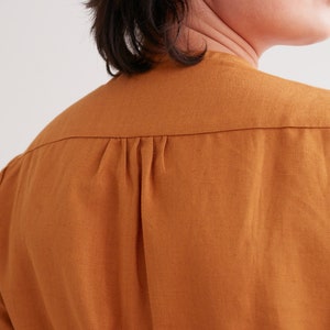 Pu&ograve; includere: Primo piano del retro di una camicia marrone a maniche lunghe con un solo piega nella schiena.