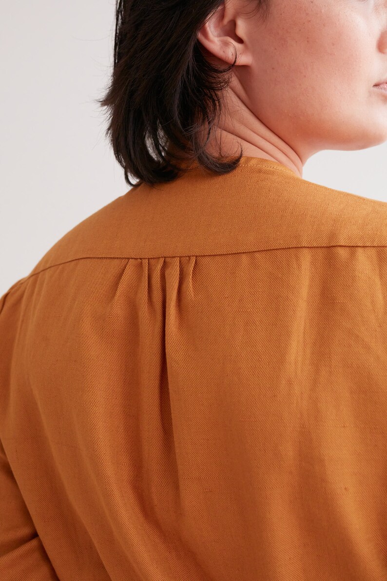 Pu&ograve; includere: Primo piano del retro di una camicia marrone a maniche lunghe con un solo piega nella schiena.