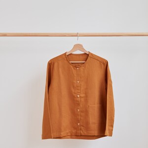 Pu&ograve; includere: Una camicia a maniche lunghe abbottonata di colore marrone caldo. La camicia ha un collo rotondo e una singola tasca a toppa sul lato sinistro.
