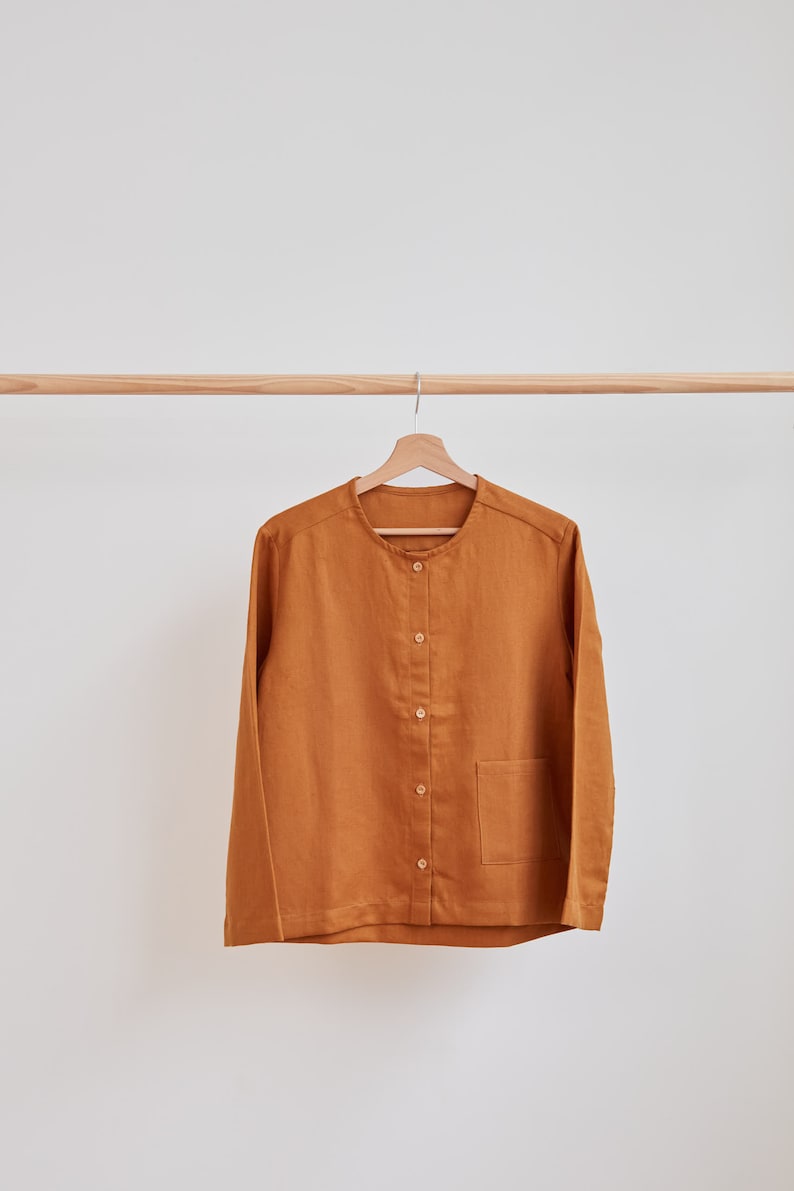 Pu&ograve; includere: Una camicia a maniche lunghe abbottonata di colore marrone caldo. La camicia ha un collo rotondo e una singola tasca a toppa sul lato sinistro.