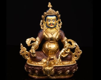 May include: A golden statue of a seated figure with intricate details. The statue has a serene expression, a crown, and ornate jewelry. The figure is seated on a detailed base, with a dark background.