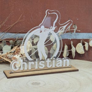 Könnte beinhalten: Eine weiße Acrylplatte mit einer Silhouette eines Bogenschützen, der einen Pfeil schießt. Die Platte steht auf einem Holzsockel und trägt den Namen "Christian".