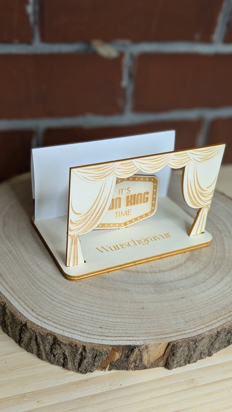 Peut inclure: Un porte-cartes en bois avec une d&eacute;coupe en forme de rideau de sc&egrave;ne et une pancarte indiquant "It's on King Time". Le porte-cartes est pos&eacute; sur une surface en bois.