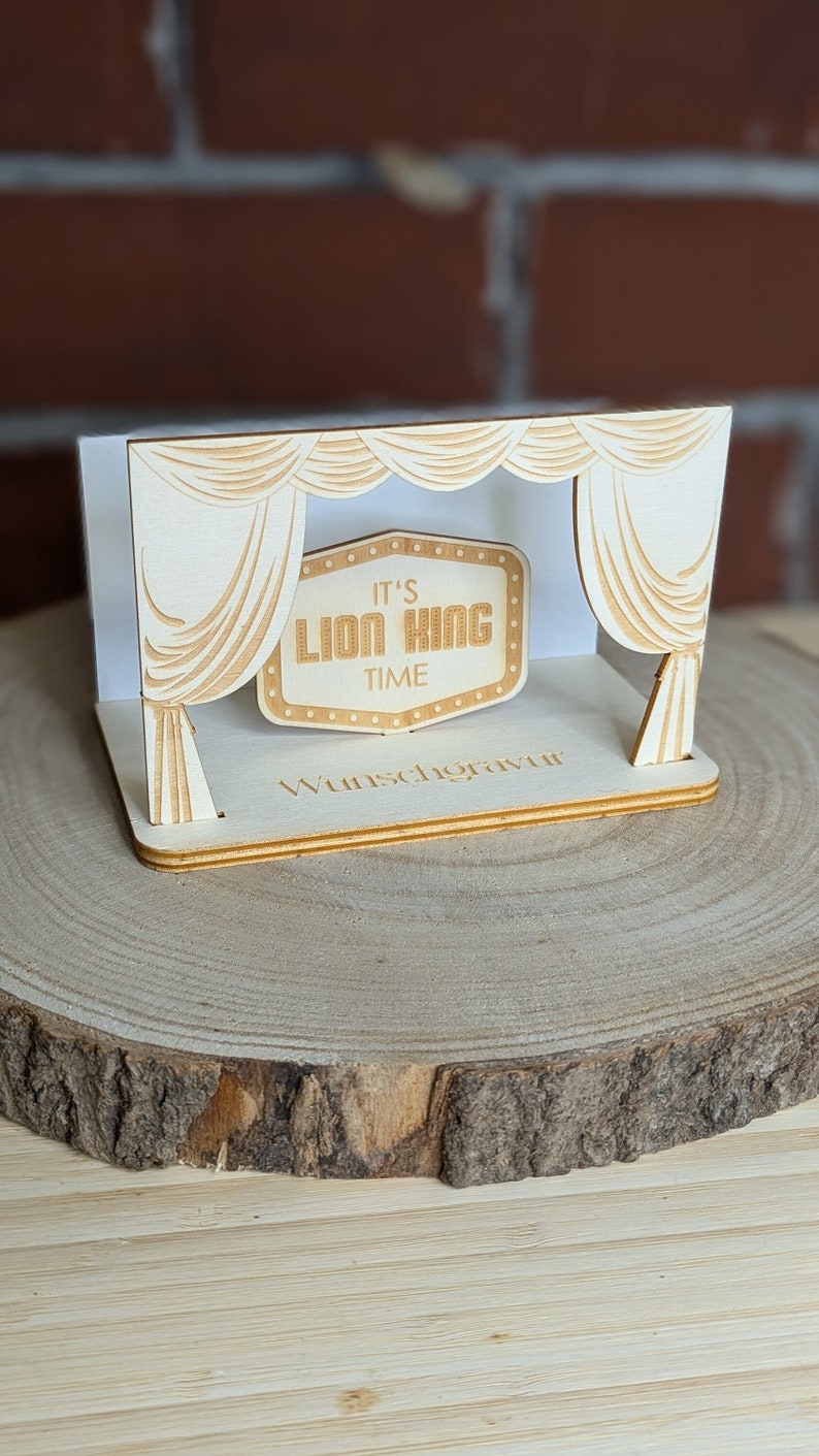 Peut inclure: Une d&eacute;coupe en bois d'une sc&egrave;ne avec des rideaux et une pancarte qui dit "It's Lion King Time". La d&eacute;coupe est sur une tranche de bois.