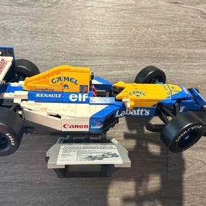 May include: A blue, yellow, and white race car model with sponsor logos, including "Labatt's", "Camel", and "Renault". The model has black wheels and is displayed on a stand. The number "5" is visible on the side.