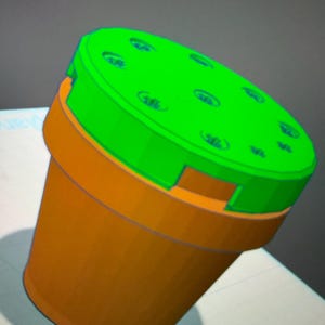 Peut inclure: Un récipient orange et vert rendu en 3D, avec un couvercle vert percé de plusieurs petites indentations circulaires. Le récipient est cylindrique, plus large en haut. Il s'agit d'une représentation numérique.