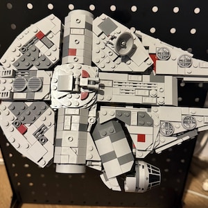 Puede incluir: Un modelo de nave espacial hecho de bloques de construcción de plástico gris y gris oscuro, con un casco principal circular, una sección de cabina rectangular y una pequeña antena parabólica. Incluye detalles en rojo y ventilaciones.