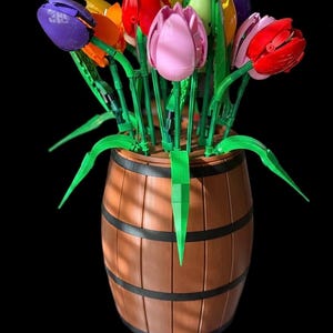 May include: A vibrant bouquet of tulip flowers in purple, orange, yellow, red, and pink. The flowers are displayed in a brown barrel-shaped vase with black bands. Green stems and leaves complete the floral arrangement.
