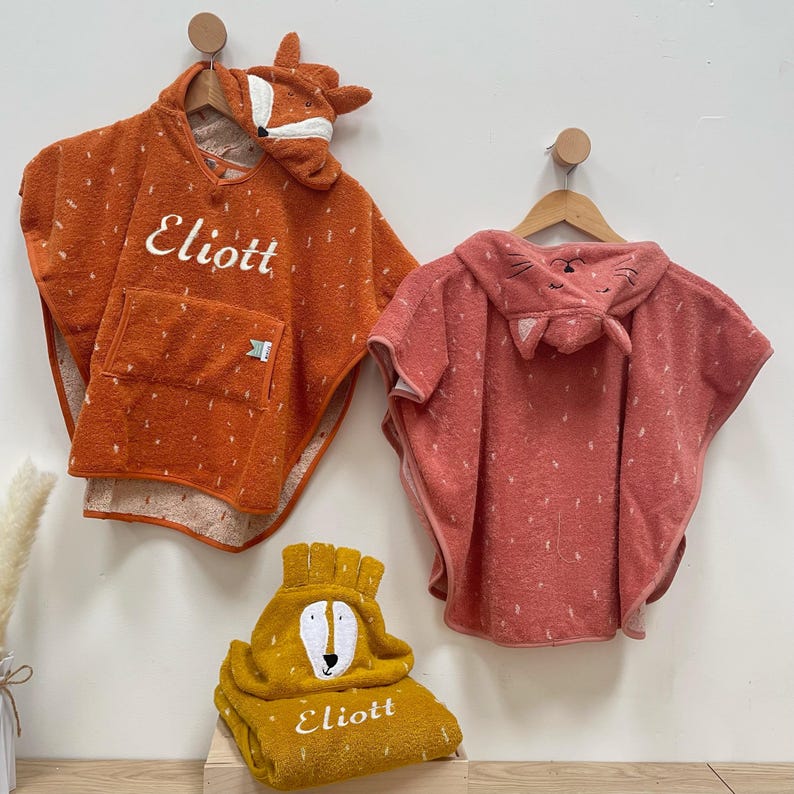 May include: Two hooded towels with animal faces, one orange with a fox face and the other pink with a cat face. A third towel is folded with a bear face and the name "Eliott" embroidered on it.