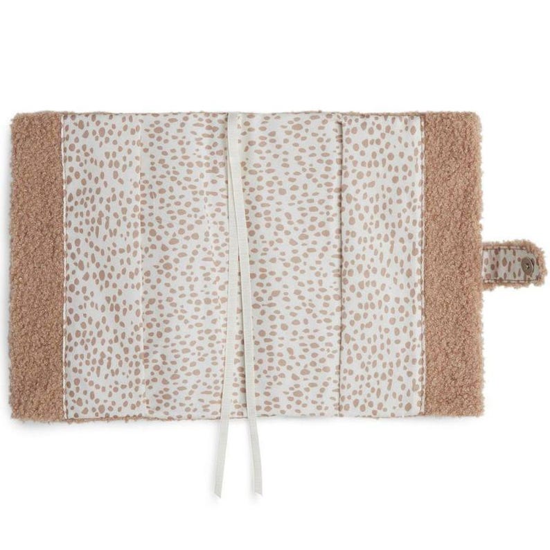 May include: A beige faux fur journal cover with a white and beige spotted lining. The cover has a white ribbon closure and a beige faux fur flap with a snap closure.