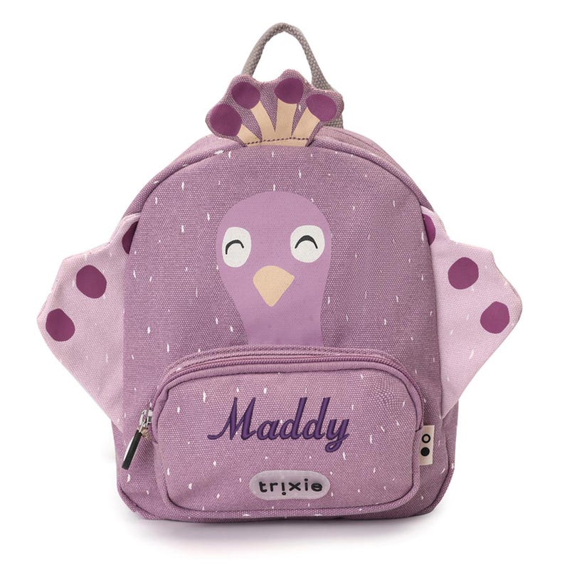 May include: A purple backpack with a bird design, featuring a front pocket with the name "Maddy" in cursive. The backpack has a handle and wings with purple polka dots. The brand name "trixie" is printed on the front pocket.