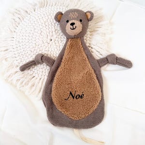 May include: A brown and gray knitted bear security blanket with a brown fuzzy belly. The blanket has a loop for hanging and the name "No&eacute;" embroidered on the belly.