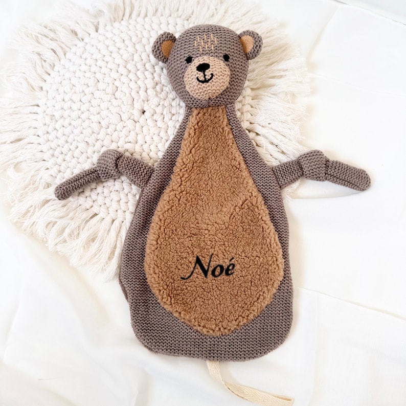 May include: A brown and gray knitted bear security blanket with a brown fuzzy belly. The blanket has a loop for hanging and the name "No&eacute;" embroidered on the belly.