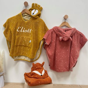 May include: Three hooded towels for children, one yellow with the name "Eliott" embroidered on it, one pink with a cat face on the hood, and one orange with a fox face on the hood.