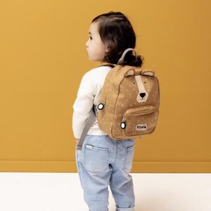 May include: A tan and white polka-dot backpack with a bear face design. The backpack has a front pocket, bear ears, and the brand name "trixie" printed on the front. The backpack is being worn by a child.