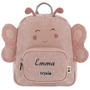 May include: A pink backpack with a butterfly design. The backpack features a smiling face, antennae, and butterfly wings. The name "Emma" is printed on the front pocket, with the brand name "trixie" below it. The backpack has a top handle and a zipper closure.