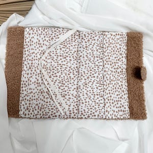 May include: A brown faux fur notebook with a white and brown spotted fabric lining. The notebook has a white ribbon bookmark.