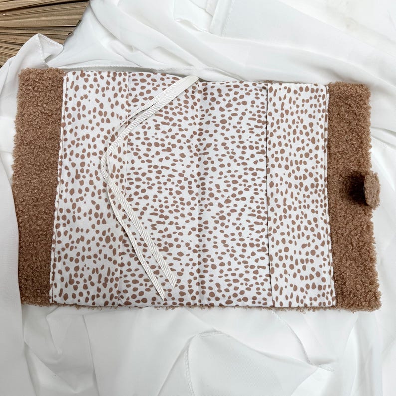 May include: A brown faux fur notebook with a white and brown spotted fabric lining. The notebook has a white ribbon bookmark.