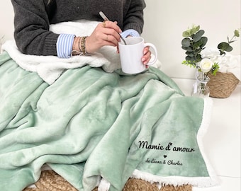 May include: A soft, green and white blanket with a white sherpa lining. The blanket has the text "Mamie d'amour de Leana & Charles" embroidered on it.