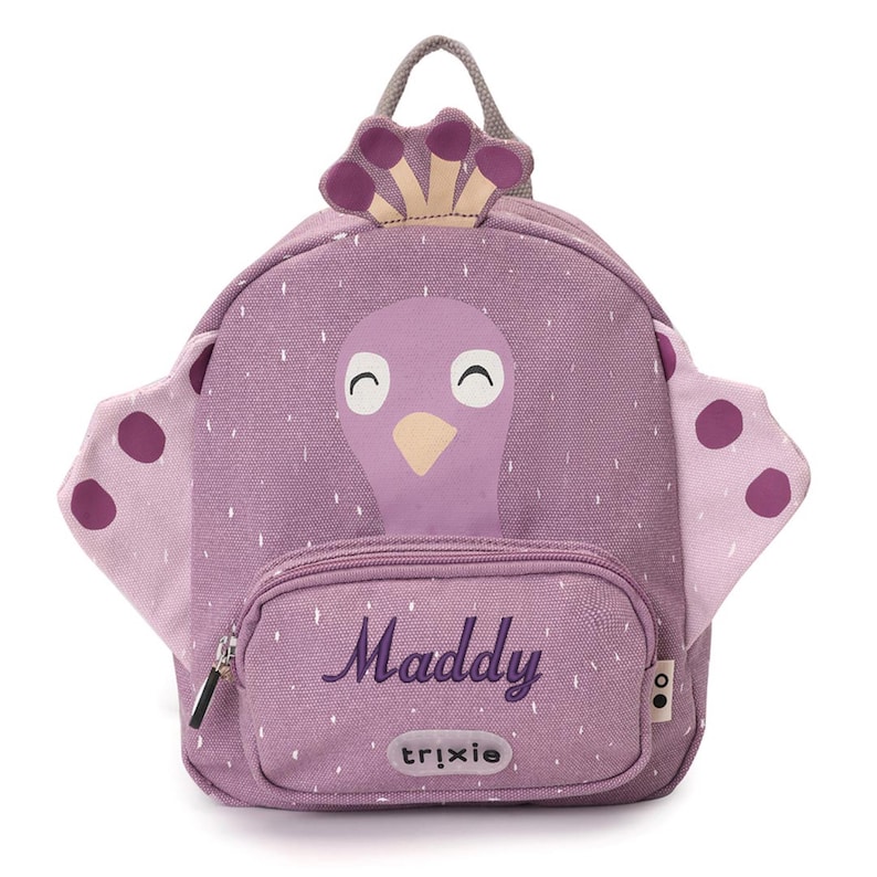 May include: A purple backpack with a bird design, featuring a front pocket with the name "Maddy" in cursive. The backpack has a handle and wings with purple polka dots. The brand name "trixie" is printed on the front pocket.