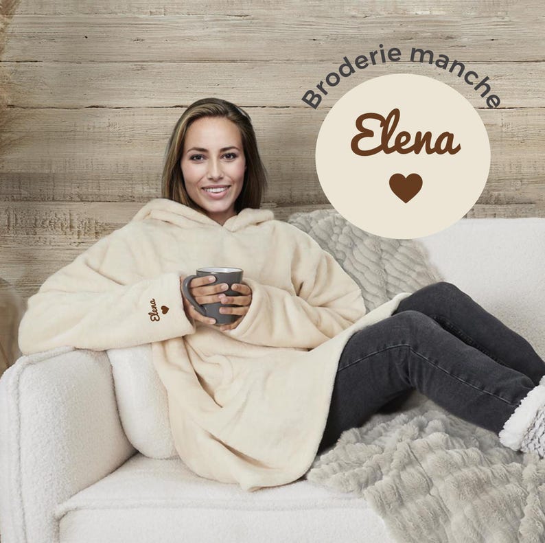 May include: A cream-colored hooded blanket with the word "Elena" embroidered on the sleeve and a heart. The blanket is worn by a person sitting on a couch.