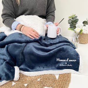May include: A blue fleece blanket with a white sherpa trim. The blanket has the text "Maman d'amour de Leana & Charles" embroidered on it.
