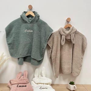 Könnte beinhalten: Zwei Kapuzenhandtücher mit Hasenohren-Kapuzen, eines grün mit dem Namen "Callie" bestickt und eines beige. Zwei kleinere Kapuzenhandtücher mit Hasenohren, eines rosa mit dem Namen "Emma" bestickt und eines weiß mit dem Namen "Laura" bestickt.