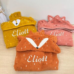 May include: Three hooded towels with animal faces. The towels are yellow, orange, and pink. Each towel has the name "Eliott" embroidered on it.
