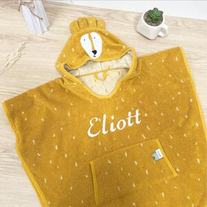 May include: A yellow hooded towel with a white embroidered deer face on the hood and the name "Eliott" embroidered on the front. The towel has a small pocket on the bottom right side.