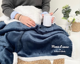 May include: A blue fleece blanket with a white sherpa trim. The blanket has the text "Mamie d'amour de Léana & Charles" embroidered on it.