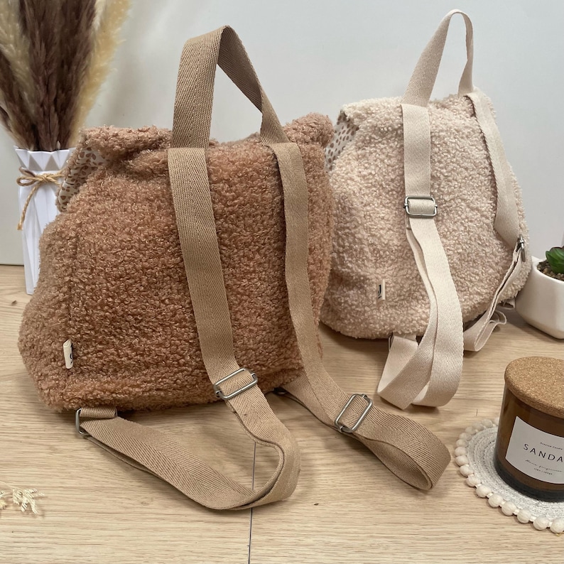 May include: Two fuzzy brown and cream-colored mini backpacks with adjustable straps. The backpacks are made of a soft, plush material.