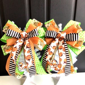 May include: Two decorative bows featuring a mix of ribbons with orange pumpkins, black and white stripes, lime green polka dots, and leopard print accents. The bows are constructed from multiple layers of wired ribbon, creating a full, voluminous shape.