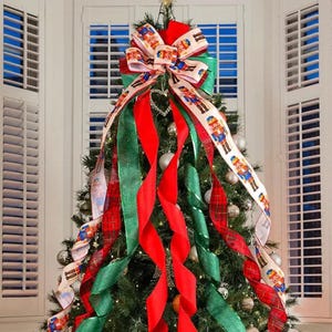 Pode incluir: Uma árvore de Natal decorada com fita vermelha e verde, uma fita branca com estampa de quebra-nozes e um grande laço vermelho e branco no topo.