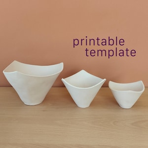 Può includere: Tre ciotole in ceramica bianca di dimensioni diverse disposte in fila, ciascuna con una base quadrata che si allarga verso un bordo curvo a quattro punte. Il testo "printable template" è visualizzato in lettere viola sopra le ciotole.