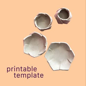Pode incluir: Quatro objetos de cor clara em forma de taça com bordas dobradas semelhantes a pétalas, dispostos em grupo. Os objetos têm um acabamento liso e mate, e um design simples e aberto. O texto "printable template" é visível no canto inferior esquerdo.