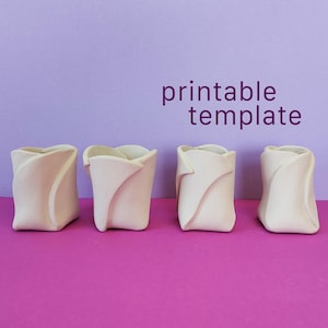 Puede incluir: Cuatro recipientes esculturales de color blanco roto con acabado mate y bordes plegados en forma de pétalo, dispuestos en fila. El texto "printable template" aparece en morado sobre los objetos. Cada recipiente tiene una silueta curva.