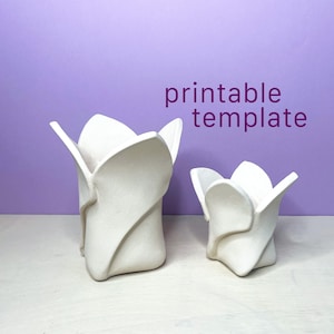 Könnte beinhalten: Zwei weiße Keramikgefäße mit einem skulpturalen, blütenblattartigen Design, das die Form einer sich öffnenden Blume nachahmt. Die Objekte sind matt und strukturiert. Der Text "printable template" steht in Lila über den zwei weißen Objekten.