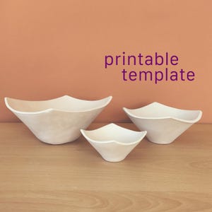 Peut inclure: Trois bols blancs avec un bord carré et des côtés incurvés, disposés en groupe. Le texte "printable template" est affiché en lettres violettes au-dessus des bols. Les bols ont une finition mate lisse et un design cohérent.