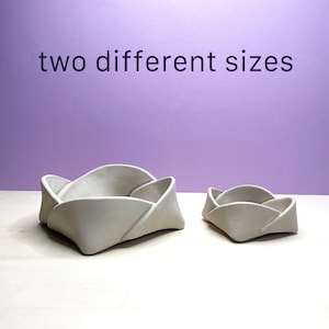 May include: Two gray, folded-petal shaped bowls in different sizes. The larger bowl is on the left, and the smaller bowl is on the right. The text "two different sizes" is above the bowls.