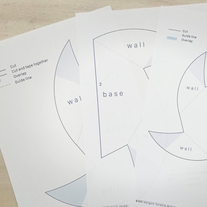 May include: Several white paper sheets with black line drawings and text, including "wall" and "base." The sheets also feature instructions: "Cut," "Cut and tape together," "Overlap," and "Guide line."