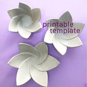 May include: Three silver-coloured, five-petaled flower-shaped bowls arranged on a purple surface. The text "printable template" is written in purple letters between the bowls. Each bowl features a smooth, curved design with pointed petals.
