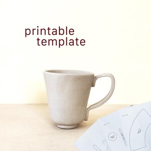 Puede incluir: Una taza de cerámica beige con un asa curva. La taza tiene una base ancha y se estrecha hacia arriba. Las palabras "printable template" están en texto granate encima de la taza. Varias plantillas de papel impresas son visibles a la derecha de la taza.