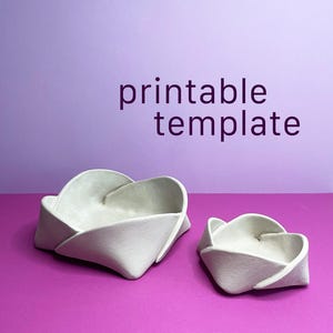 Può includere: Due ciotole di carta piegata bianco sporco su una superficie viola, con uno sfondo lavanda. La ciotola più grande è in primo piano, con la ciotola più piccola a destra. Il testo "printable template" è sullo sfondo.