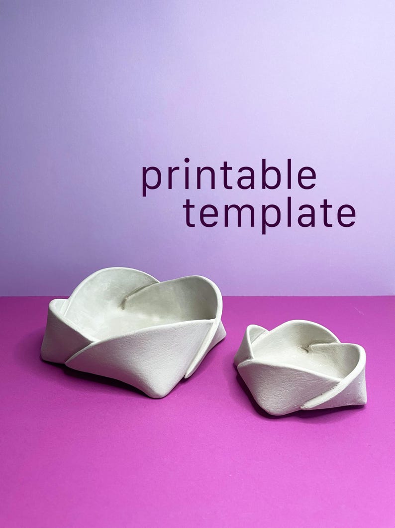 May include: Two off-white, folded paper bowls on a purple surface, with a lavender background. The larger bowl is in the foreground, with the smaller bowl to the right. The text "printable template" is in the background.